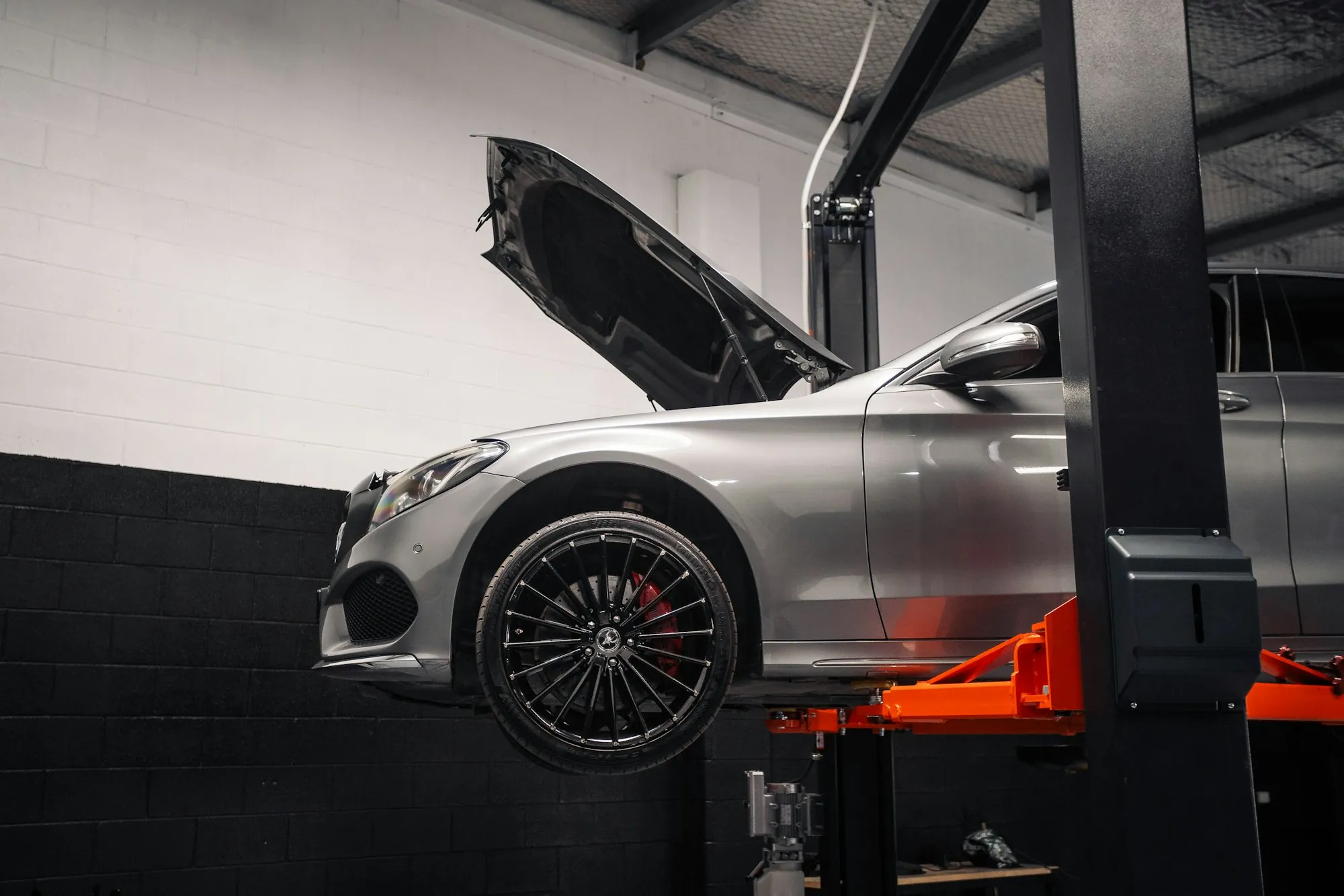 Silver sedan raised on a lift with its hood open in a shop